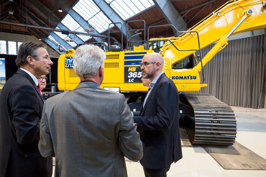 Voorzitter Maxime Verhagen van Bouwend Nederland (links) krijgt uitleg van Patrick Schothuis (BIA Group) over de werking van de Komatsu HB 365 LC Hybrid. BIA had de machine meegenomen om op de informatiemarkt, een onderdeel van de BouwMachines Kennisdag, te laten zien. 