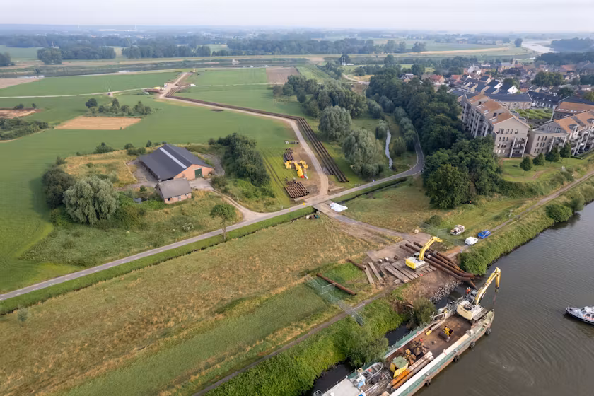 Om te voorkomen dat het water voor de tijdelijke dam stagneert is een hevelleiding aangelegd richting de Maas (achtergrond). Foto: Rijkswaterstaat / LimburgDrone.